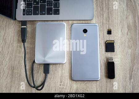 Laptop and mobile phone data transfer peripherals - portable HDD, usb flash drive and SD cards - lying on a wooden table. Stock Photo