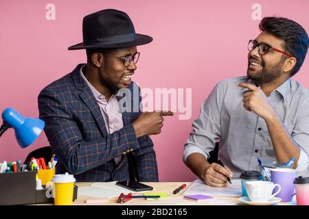 Two confident and cheerful business partners having funny conversations discussing plans, sharing ideas, sitting at table with papers, drinking coffee Stock Photo