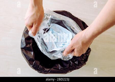 Throwing away single use medical face mask. Packing it in one time plastic bag before throwing it in trash to prevent virus from spreading from mask t Stock Photo