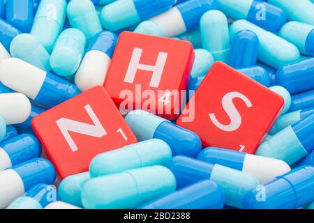 NHS letters tiles sinking into pills. For NHS overwhelmed by Covid 19 pandemic, NHS heroes, National Health Service, NHS struggling under covid cases