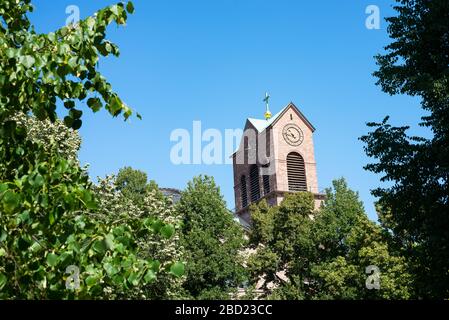 Karlsruhe, Germany - July 27, 2018. Old clock on the bell tower of St. Stephan Church among green trees tops on a background of clear blue sky in city Stock Photo