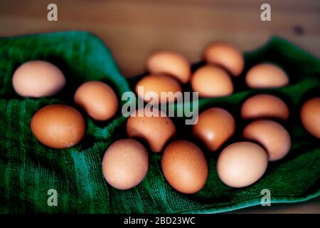 Brown fresh chicken eggs on green kitchen towel. Pile of eggs on wooden table. Concept of farm products, natural food, easter. Protein food. Selective Stock Photo