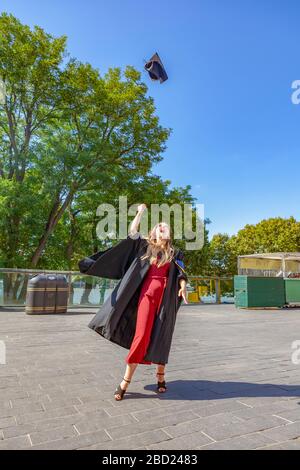 Young female graduate in London celebrating gaining a univeresity degree by throwing her mortar board high in the air Stock Photo