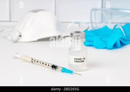 Concept of Covid-19 coronavirus drug vaccine. Medicine vial, needle syringe, medical exam gloves, safety glasses and N95 respirator mask Stock Photo