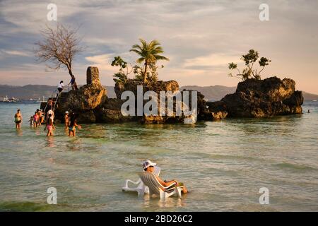 A man relaxes sitting on a chair in the water in front of Willy's Rock at the White Beach of Boracay. Stock Photo