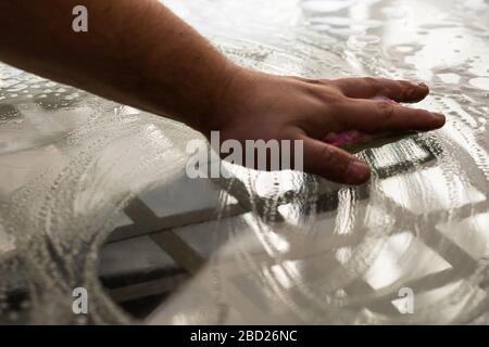 Man cleaning glass table using sponge and cleaning sprayer, cleaning services concept. Housework and housekeeping concept Stock Photo