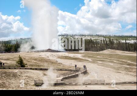 Tourists on the boardwalk watching as the famous Old Faithful Geyser erupts in Yellowstone National Park Stock Photo