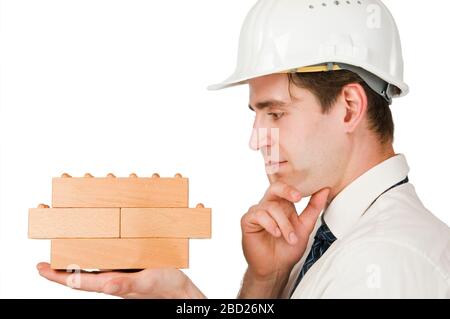Head-and-shoulder view of a young man in profile with a white shirt, tie and white construction site helmet looking thoughtfully at the wooden blocks. Stock Photo