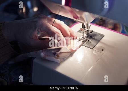 hands of a woman sewing on a machine at home, concept of manual work and hobbies, dark style and selective focus Stock Photo