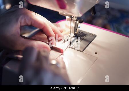 detail of the hands of an artisan woman sewing on a machine at home, concept of manual work and hobbies, dark style and selective focus Stock Photo