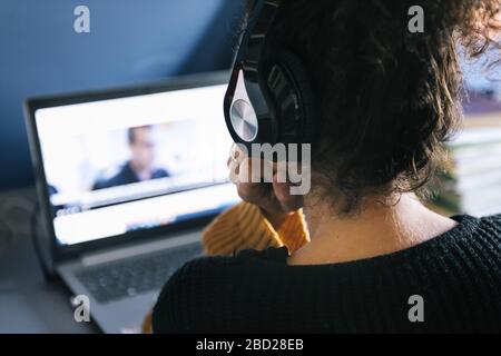rear view of a woman with headphones watching a movie on laptop at home, technology and entertainment concept, selective focus Stock Photo