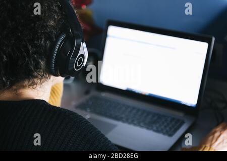 rear view of a woman listening music with headphones on laptop at home, technology and entertainment concept, selective focus Stock Photo