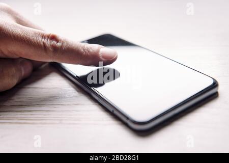 finger touching the screen of a phone with blank screen on white wooden table, technology and communication concept, selective focus Stock Photo