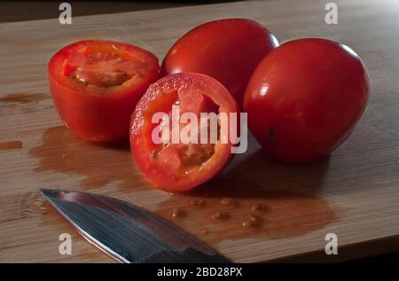 Red juicy tomatoes on a wooden cutting board with a knife on the side and with a rim light as part of macro photography or close up image Stock Photo