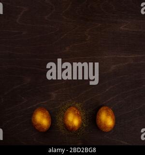 Three big golden easter eggs on dark wooden background copy space for text Stock Photo