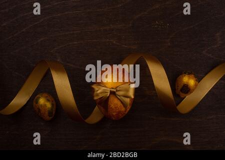 Golden luxury easter eggs and ribbon composition on dark wooden background with copy space for text card Stock Photo