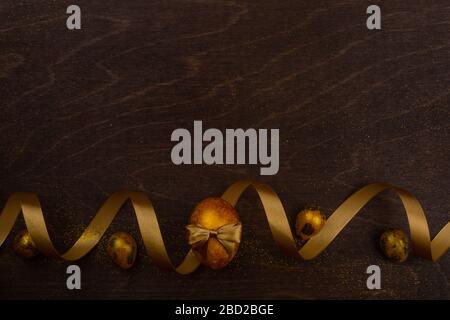 Golden luxury easter eggs and ribbon composition on dark wooden background with copy space for text card Stock Photo
