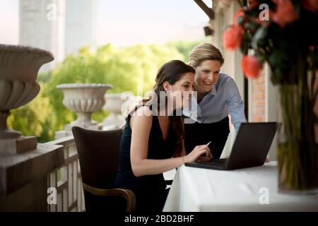 Two businesswomen using a laptop outside on a balcony. Stock Photo