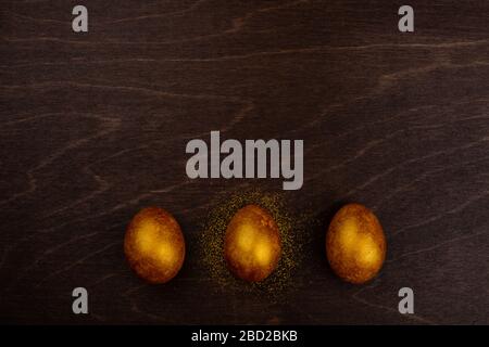 Three big golden easter eggs on dark wooden background copy space for text Stock Photo