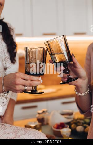 Women cheering with two black glasses. Women clinking two glasses of wine in the kitchen. Stock Photo