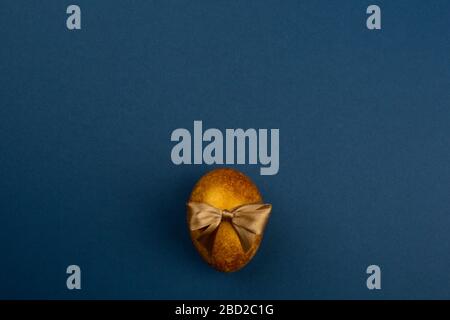 One big golden easter egg with ribbon bow on blue background copy space for text Stock Photo