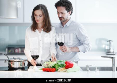 Couple drinking red wine in kitchen and cooking healthy dinner together Stock Photo