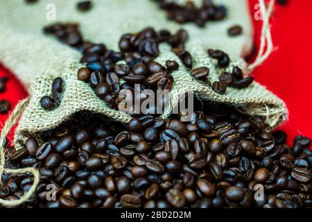 Roasted coffee beans in a burlap sack, sackcloth bag with coffee beans on red background, top view, coffee concept Stock Photo