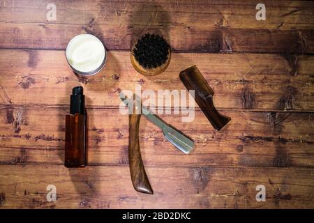 A selection of men's beard grooming products that include oil, wax and a brush, shot against a wooden background Stock Photo