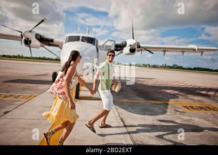 Smiling young married couple walking hand in hand toward an airplane. Stock Photo