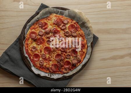 Overhead photography of a homemade pepperoni and sausage pizza on metal tray with a black napkin in a wooden table Stock Photo