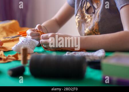 The young seamstress is sewing. Shallow depth of field. Focus on the fingers. Nearby lies a needle pad and spools of thread. Horizontal. Stock Photo