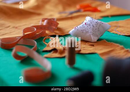 Flexible measuring tape and needle pad on the seamstress table. Seamstress tools. Shallow depth of field. Focus on the needles. Spools of thread. Stock Photo