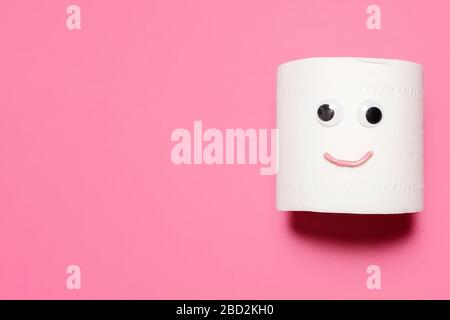 Happy smiling full roll of toilet paper with googly eyes and mouth on a pink background with copy space and room for text Stock Photo