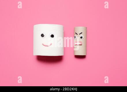 Happy smiling full roll of toilet paper next to angry empty roll with googly eyes and mouth on a pink background with copy space and room for text Stock Photo