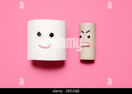 Happy smiling full roll of toilet paper next to angry empty roll with googly eyes and mouth on a pink background with copy space and room for text Stock Photo