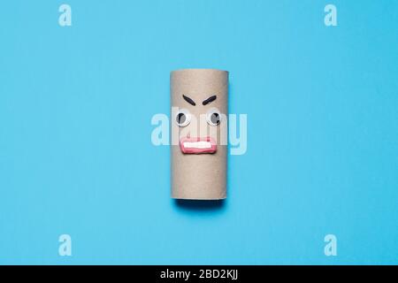 Angry empty roll of toilet paper with googly eyes, mouth and eyebrows on a blue background with copy space and room for text Stock Photo
