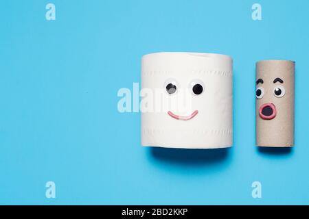 Happy smiling full roll of toilet paper next to surprised empty roll with googly eyes and mouth on a blue background with copy space and room for text Stock Photo