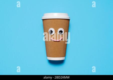 Brown paper and plastic coffee cup with google eyes and happy face on a blue background with copy space and room for text. Stock Photo