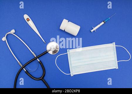 Phonendoscope, protective medical face mask and electronical thermometer on blue background Stock Photo