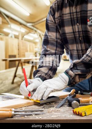 Close-up. Carpenter with his hands protected by gloves with pencil and carpenter's square draw the cutting line on a wooden board. Construction indust Stock Photo