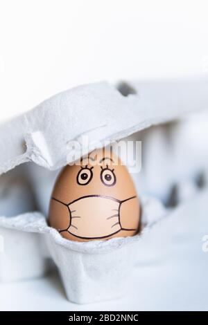 Chicken egg looking out of a tray with doodle face wearing medical mask. Conceptual image of stay at home during Corona virus quarantine Stock Photo