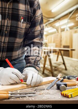 Close-up. Carpenter with his hands protected by gloves with a pencil and the meter marks the measurement on a wooden board. Construction industry, car Stock Photo
