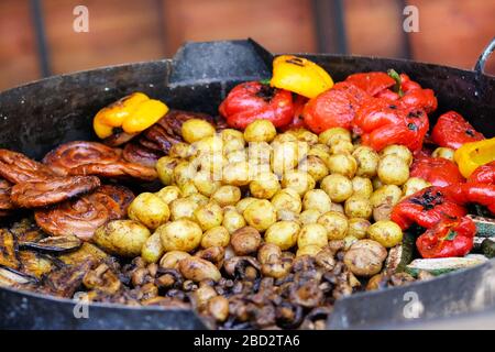 Frying pan with fried potatoes, sausages, mushrooms and pepper.Street food and outdoor cooking concept. Stock Photo