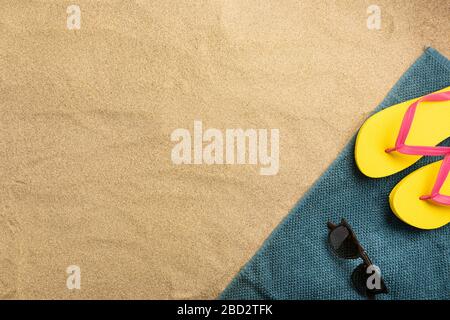Summer fashion, summer outfit on sand background. Yellow flip flops and sunglasses. Flat lay, top view Stock Photo