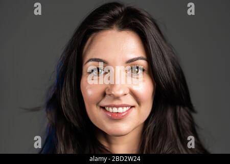 Charming mature woman isolated on grey studio background. Portrait of adult lady with long hair in blue shirt with smile looking to camera. Stock Photo