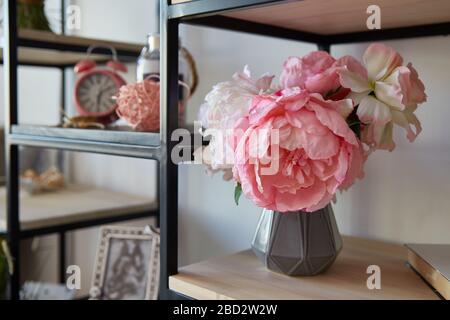 a vase with pink flowers with stands alarm clock on a shelf in the room. Interior design elements. Stock Photo