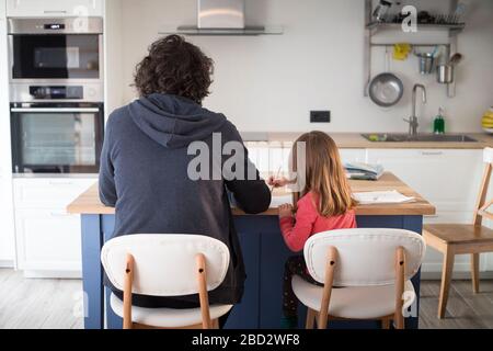 Young father working from home with little daughter during covid-19 lockdown. Child with dad smartworking in kitchen for social isolation. Stock Photo