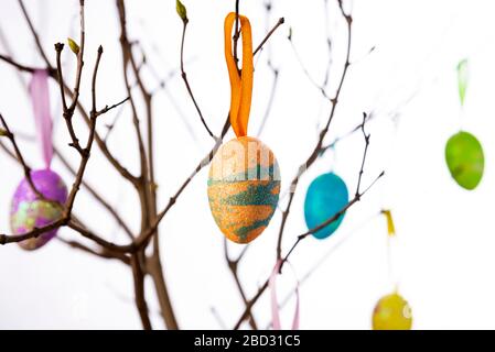 Colorful easter eggs hanging from tree branches on a light background Stock Photo