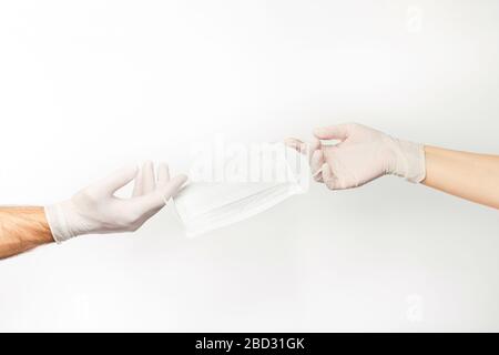 Men's and women's hands in latex gloves holding one medical mask. Stock Photo