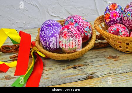 Still life with Easter eggs. Decorated Easter eggs lay in a wicker basket on a white wooden background. Easter eggs, decorated with traditional folk Stock Photo